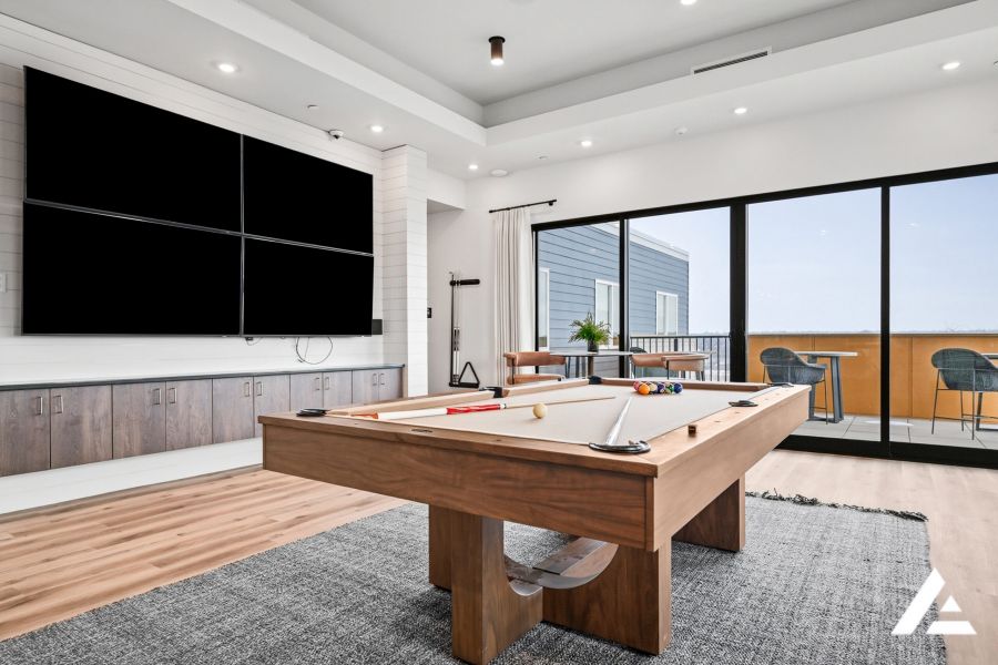Modern game room with a pool table, large TV wall, and sliding doors opening to a balcony with seating.