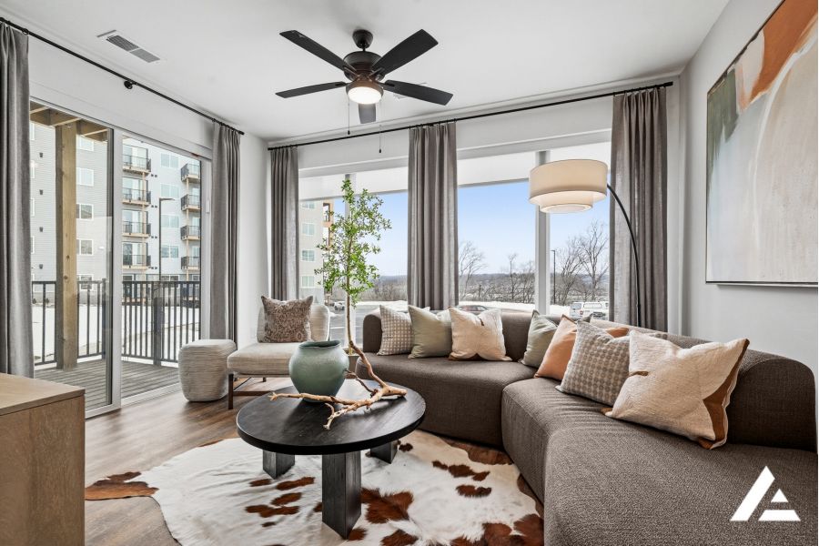 Modern living room with large windows, brown curved sofa, round table, and neutral decor accents.