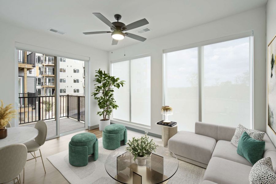 Bright modern living room with large windows, a gray sofa, round table, and balcony view.