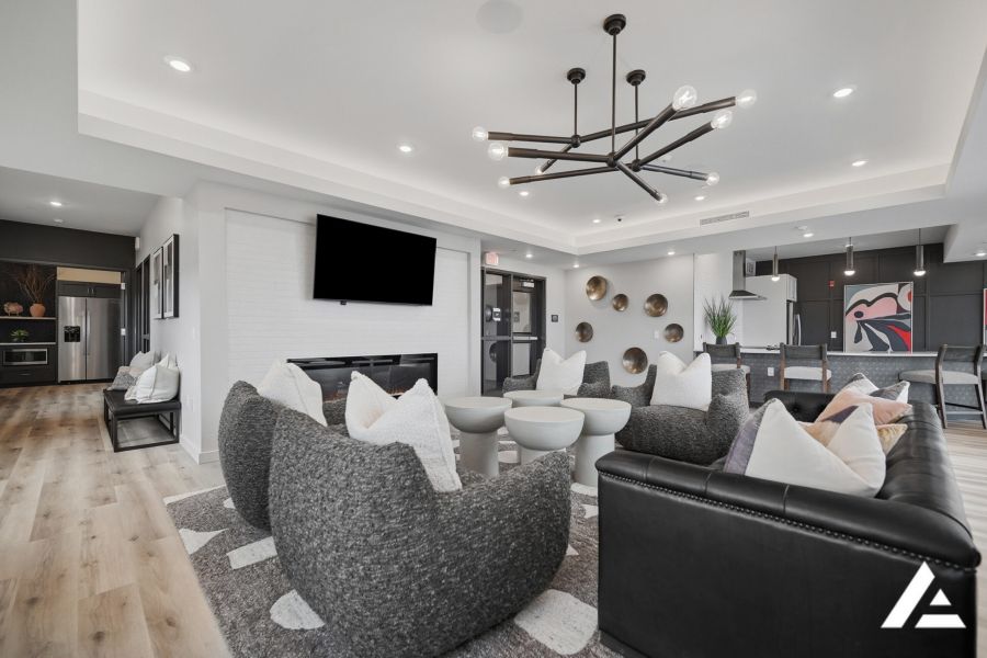 Modern lounge with black sofas, light chairs, wall-mounted TV, and contemporary lighting, featuring open kitchen.