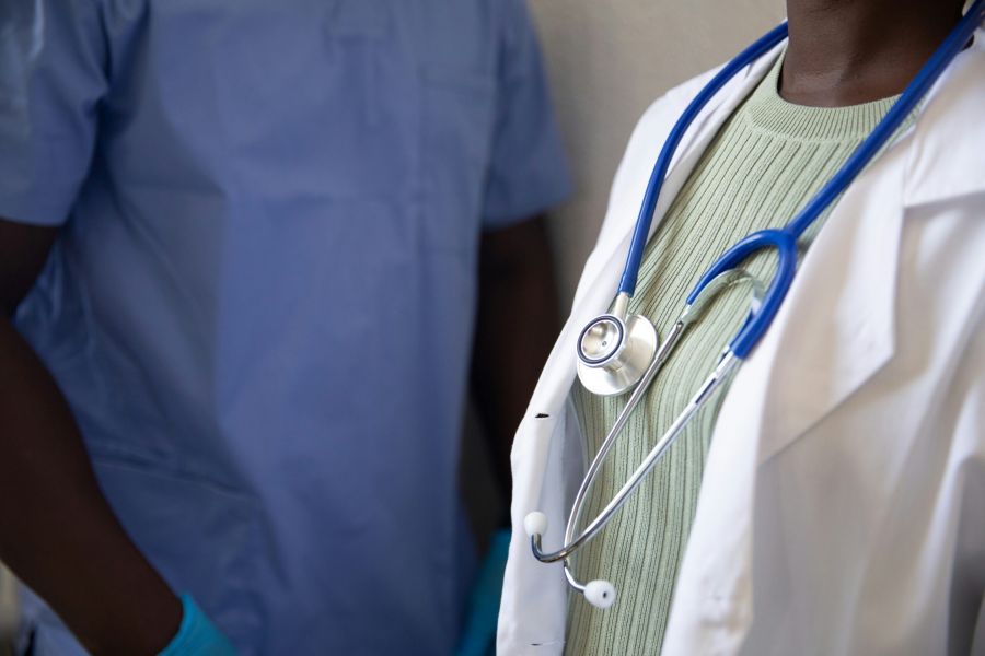 Two medical professionals, one in scrubs and one in a white coat with a stethoscope, standing together.