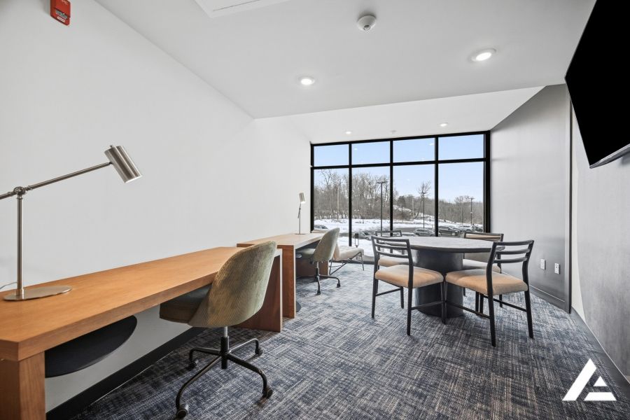 Modern office space with two desks, chairs, a round table, large window, and winter view outside.