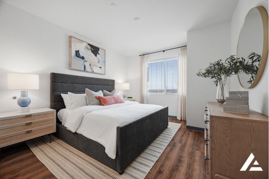 Modern bedroom with a dark bed, white bedding, two lamps, a dresser, and large window with natural light.