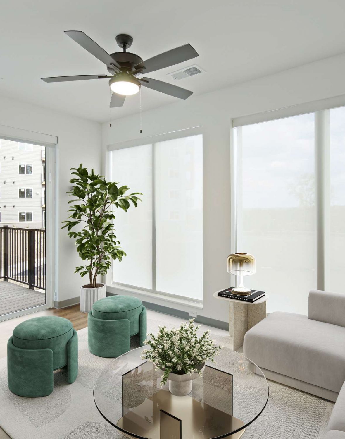 Bright modern living room with large windows, a gray sofa, round table, and balcony view.