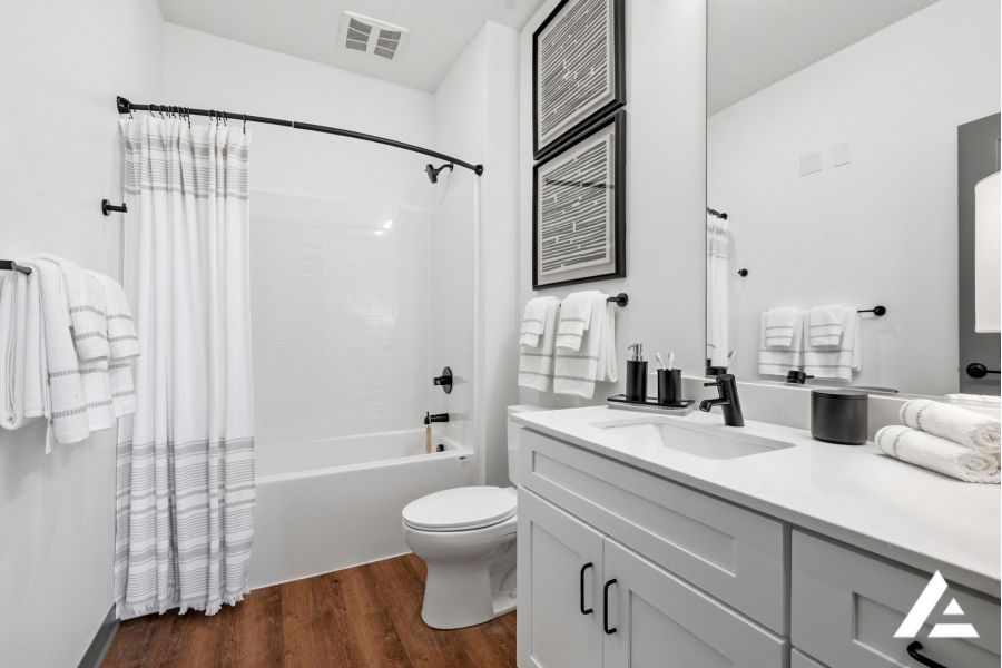 Modern white bathroom with a bathtub, striped shower curtain, double sink, and wood flooring.