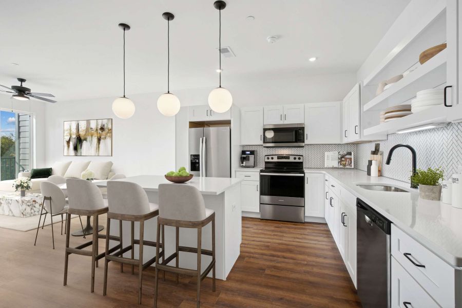 Modern white kitchen with island, bar stools, stainless steel appliances, and wood flooring.