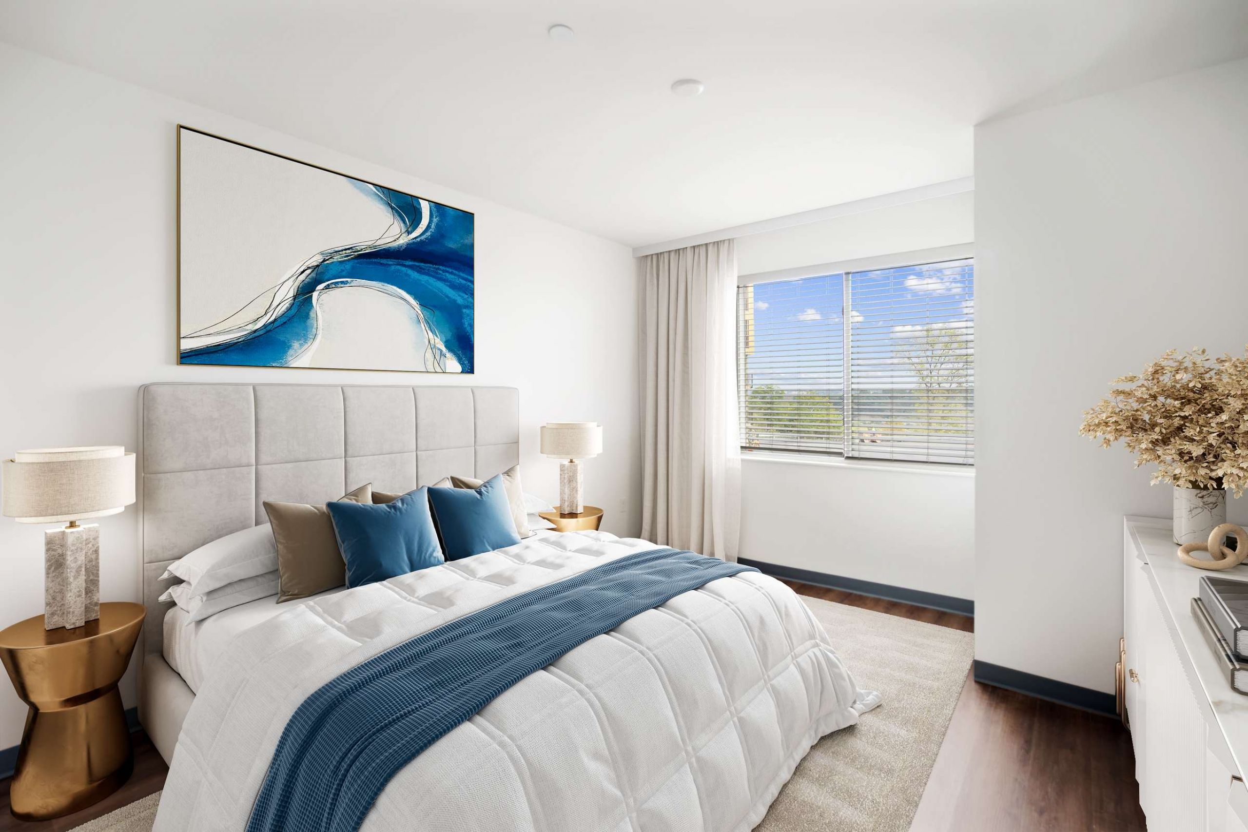 Modern bedroom with a large bed, blue accents, abstract wall art, and sunlight streaming through a window.