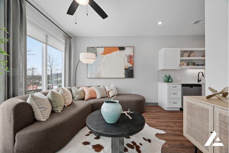 Modern living room with a curved sofa, abstract art, and a small kitchenette in neutral tones.